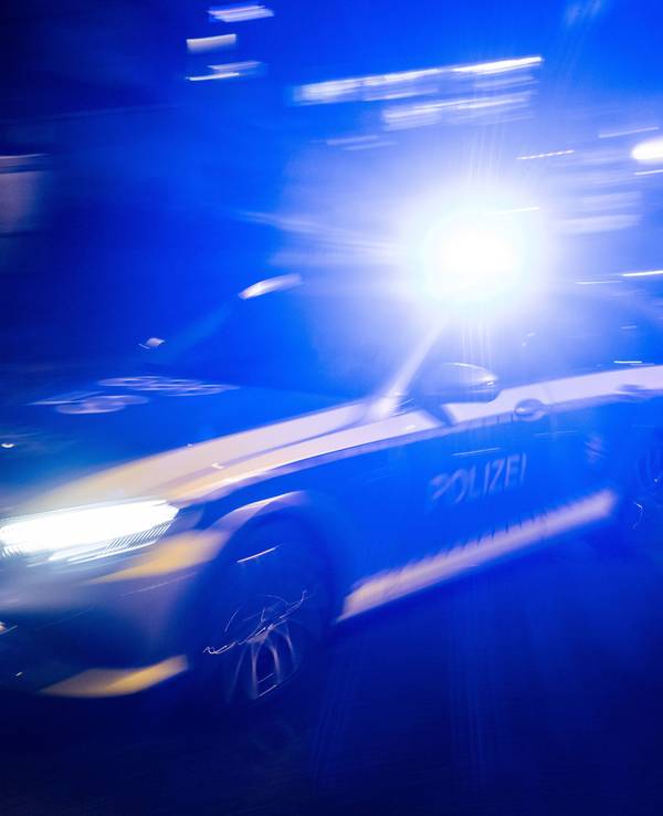 Ein Polizeifahrzeug fährt mit Blaulicht an einem Gebäude vorbei.