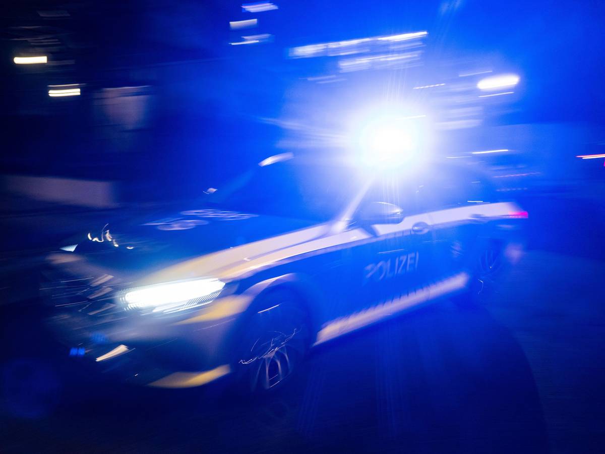 Ein Polizeifahrzeug fährt mit Blaulicht an einem Gebäude vorbei.