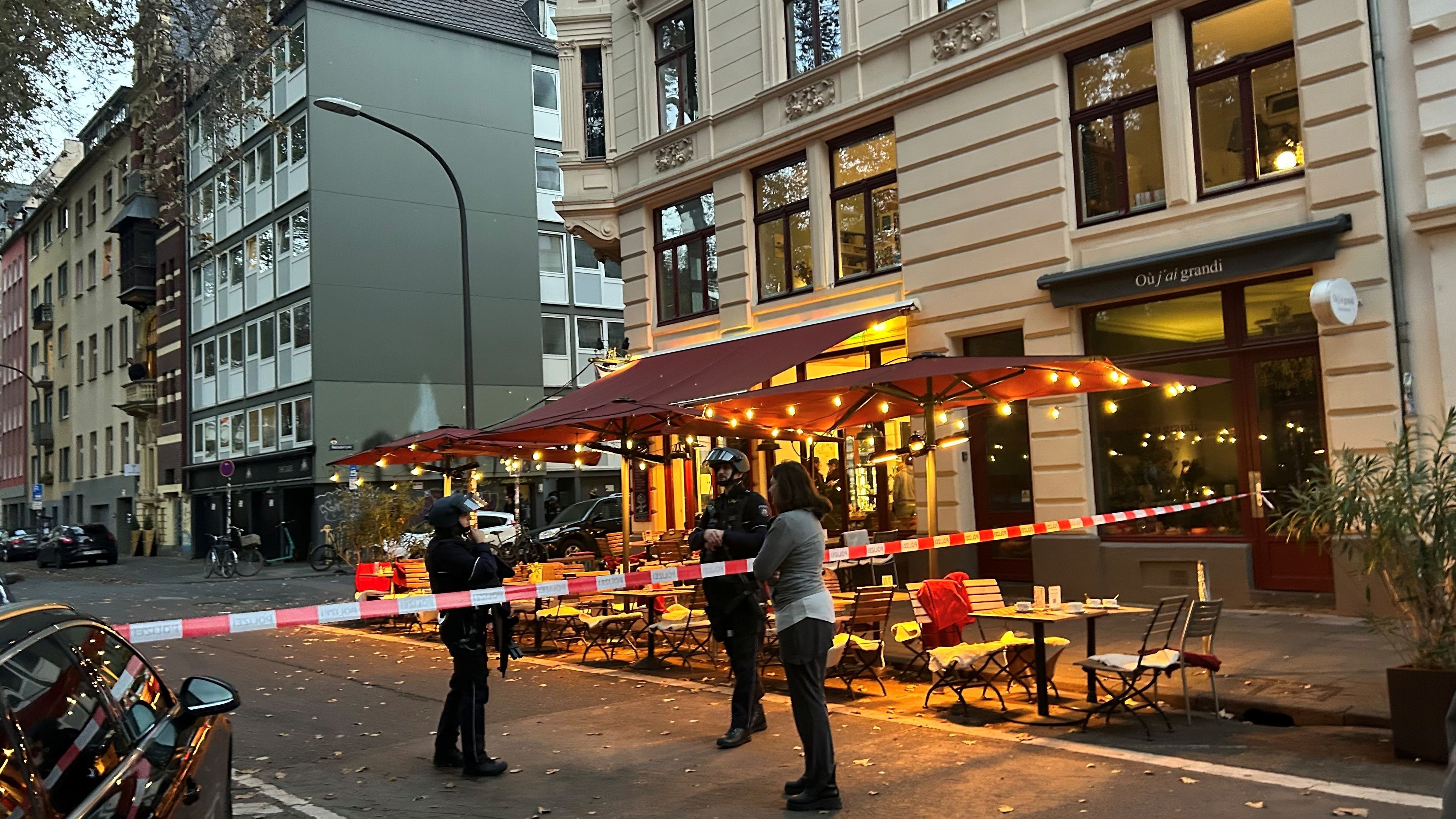 Die Polizei hat eine Straße in Höhe eines Cafés abgesperrt, zwei bewaffnete Beamte stehen hinter dem Flatterband.
