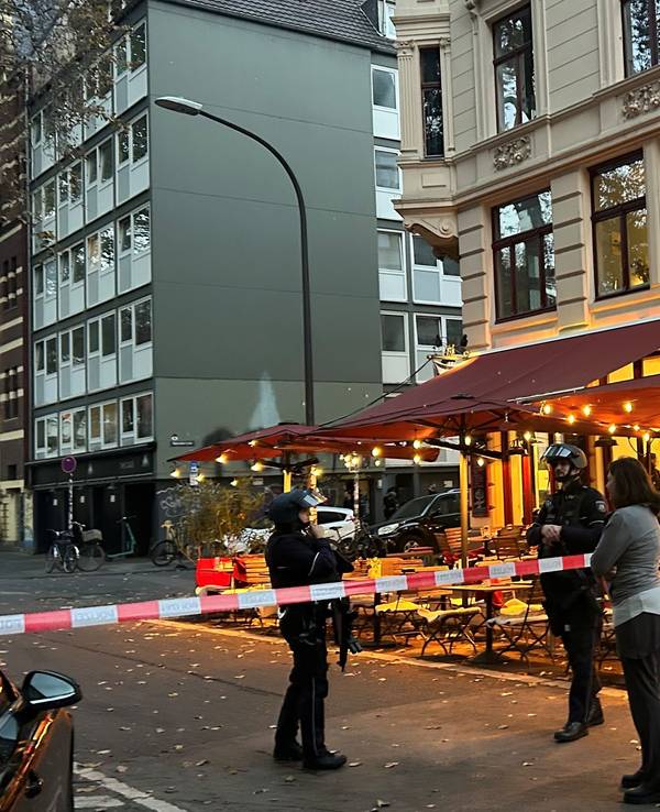 Die Polizei hat eine Straße in Höhe eines Cafés abgesperrt, zwei bewaffnete Beamte stehen hinter dem Flatterband.