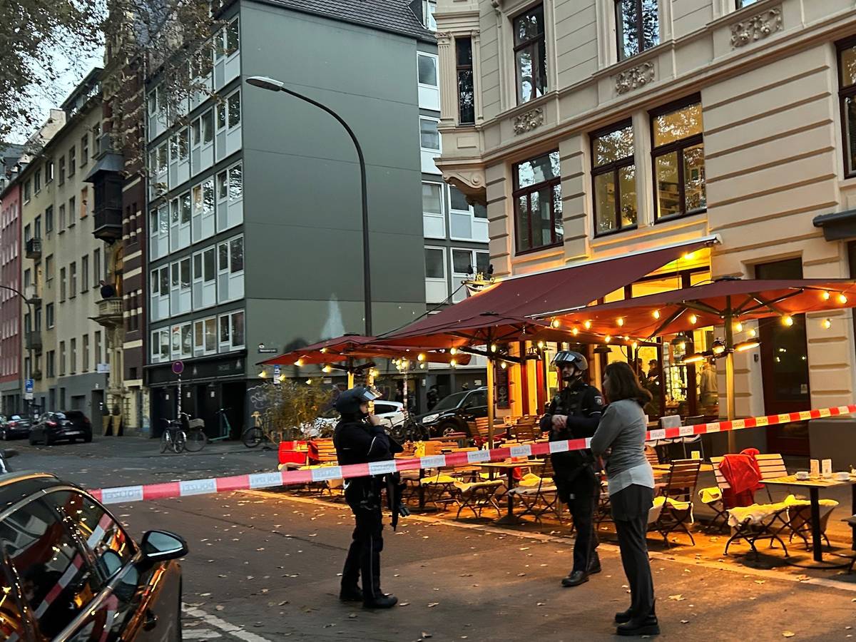 Die Polizei hat eine Straße in Höhe eines Cafés abgesperrt, zwei bewaffnete Beamte stehen hinter dem Flatterband.
