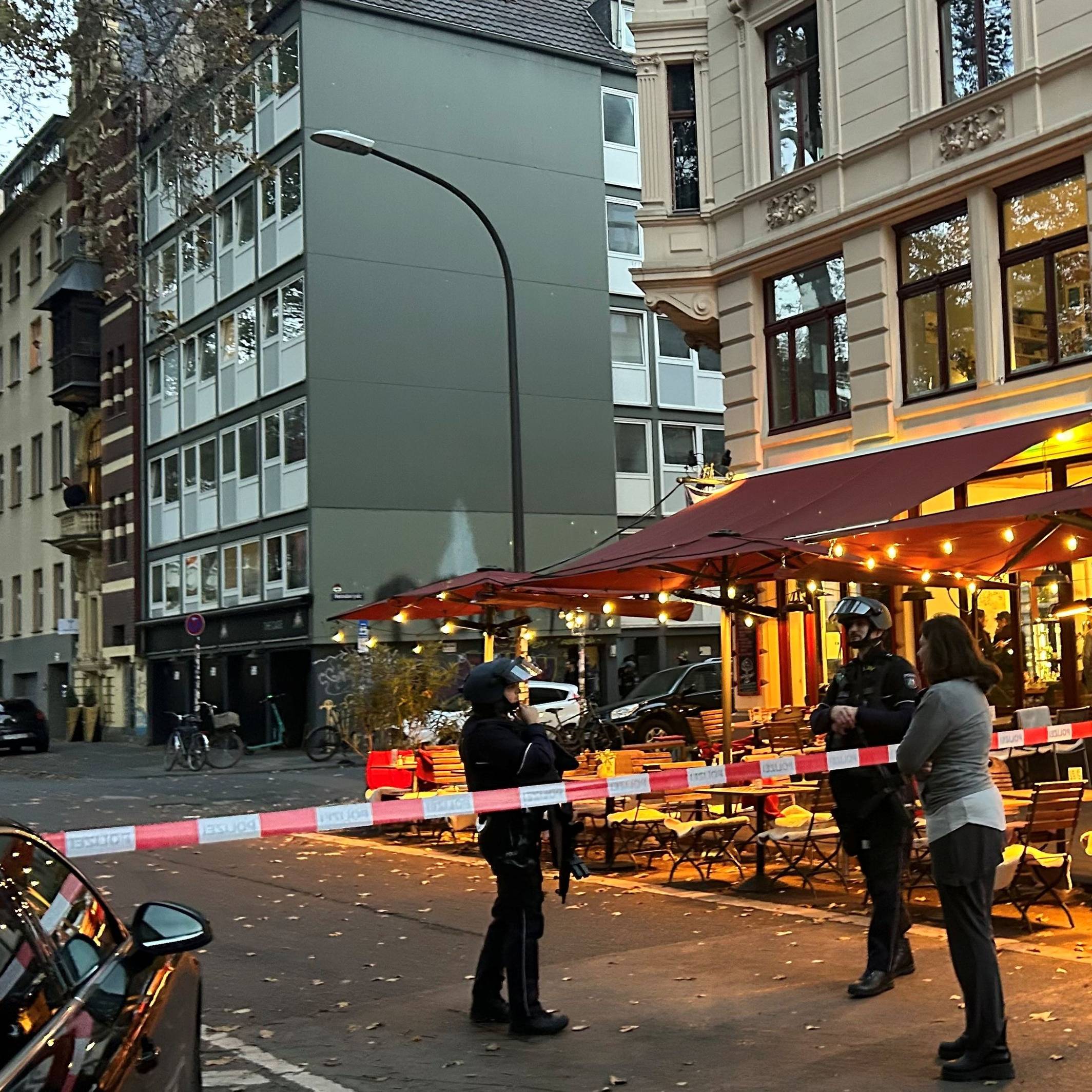 Die Polizei hat eine Straße in Höhe eines Cafés abgesperrt, zwei bewaffnete Beamte stehen hinter dem Flatterband.