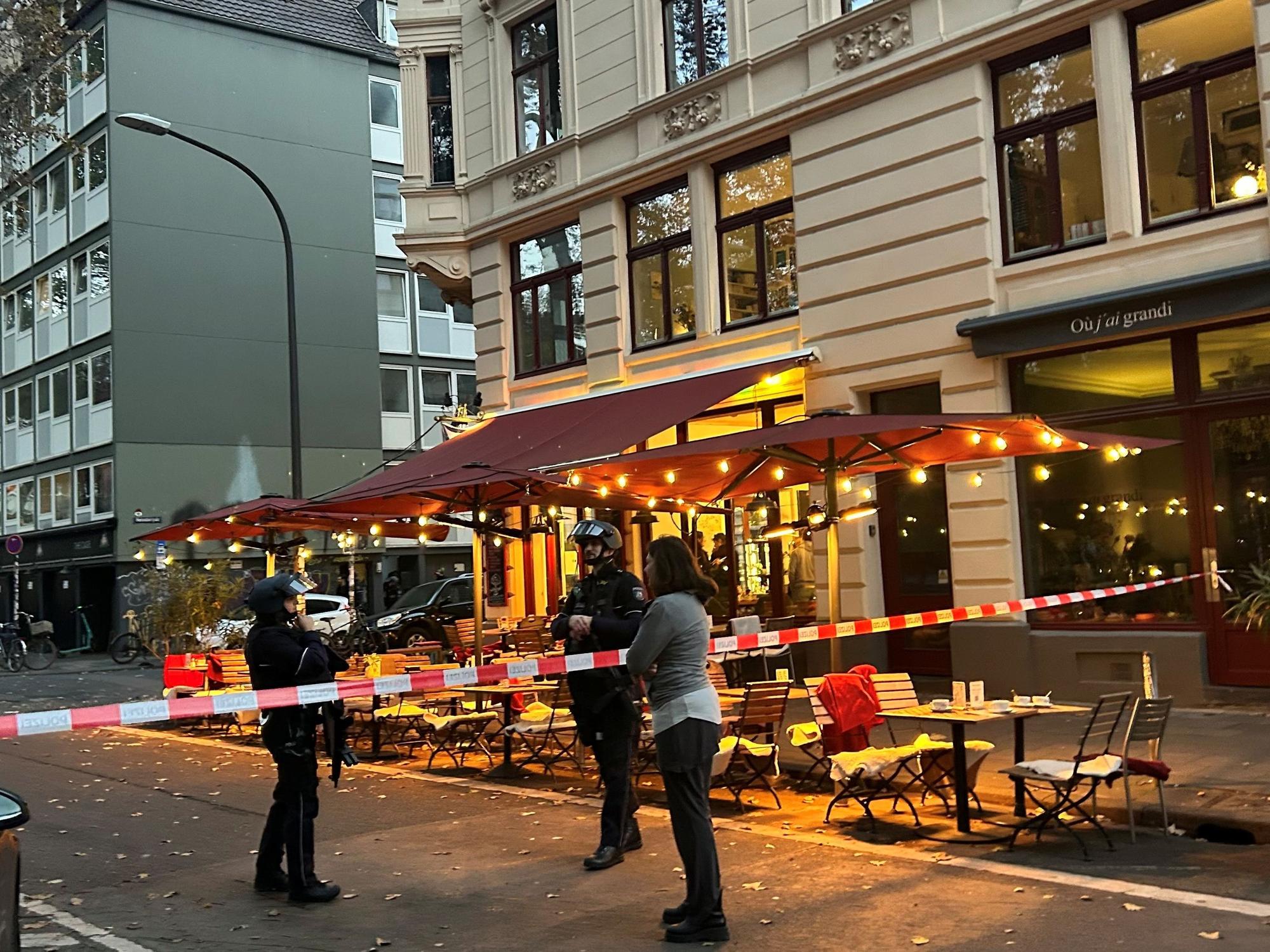 Die Polizei hat eine Straße in Höhe eines Cafés abgesperrt, zwei bewaffnete Beamte stehen hinter dem Flatterband.
