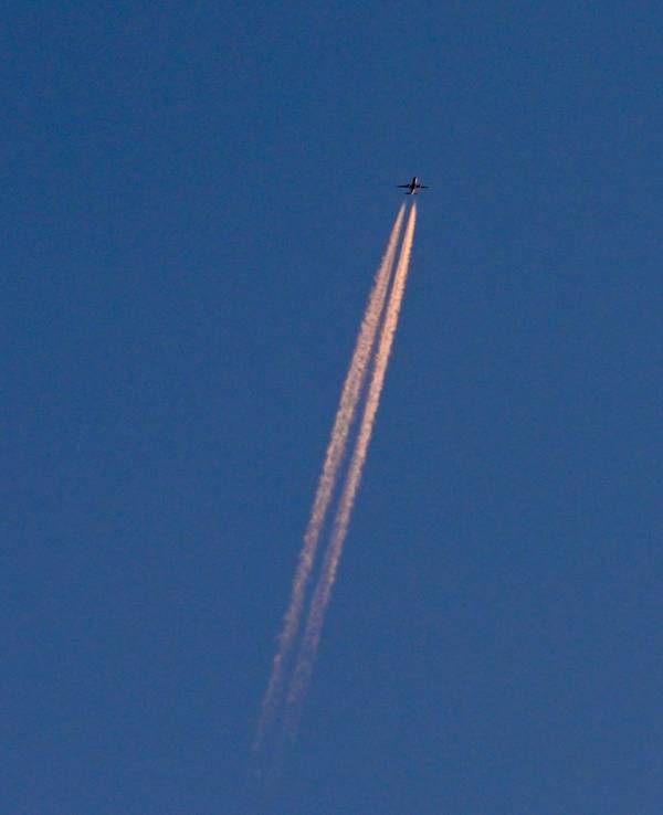 Am blauen Himmel fliegt ein Flugzeug und hinterlässt Kondensstreifen. (Symbolbild)