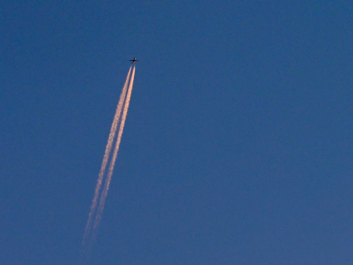 Am blauen Himmel fliegt ein Flugzeug und hinterlässt Kondensstreifen. (Symbolbild)
