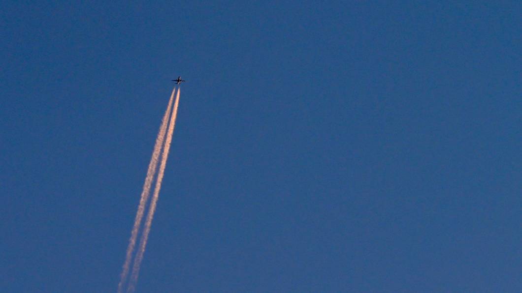 Am blauen Himmel fliegt ein Flugzeug und hinterlässt Kondensstreifen. (Symbolbild)