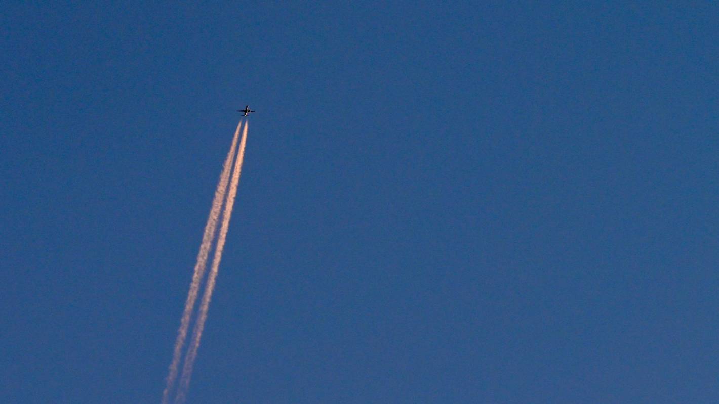 Am blauen Himmel fliegt ein Flugzeug und hinterlässt Kondensstreifen. (Symbolbild)