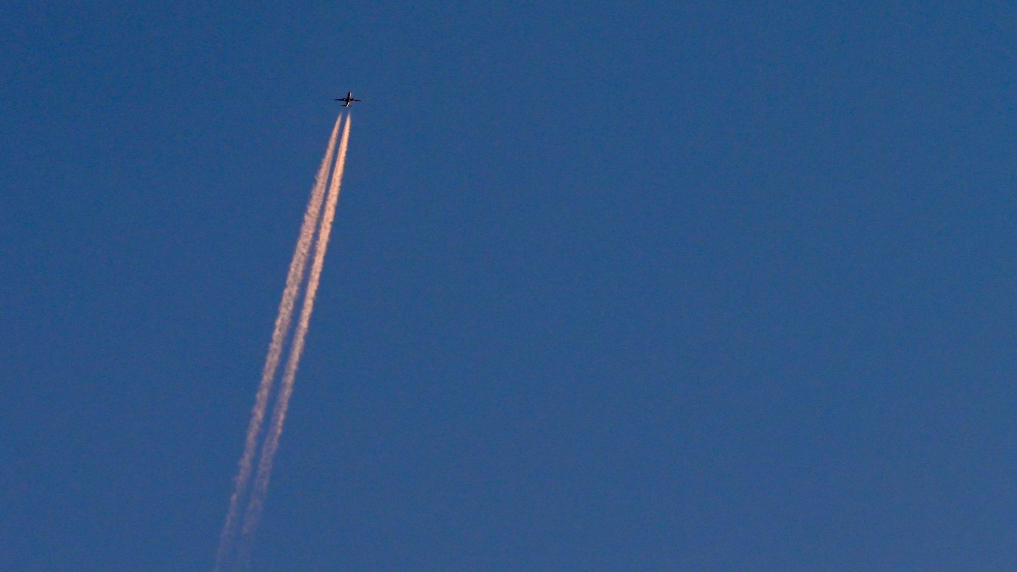 Am blauen Himmel fliegt ein Flugzeug und hinterlässt Kondensstreifen. (Symbolbild)