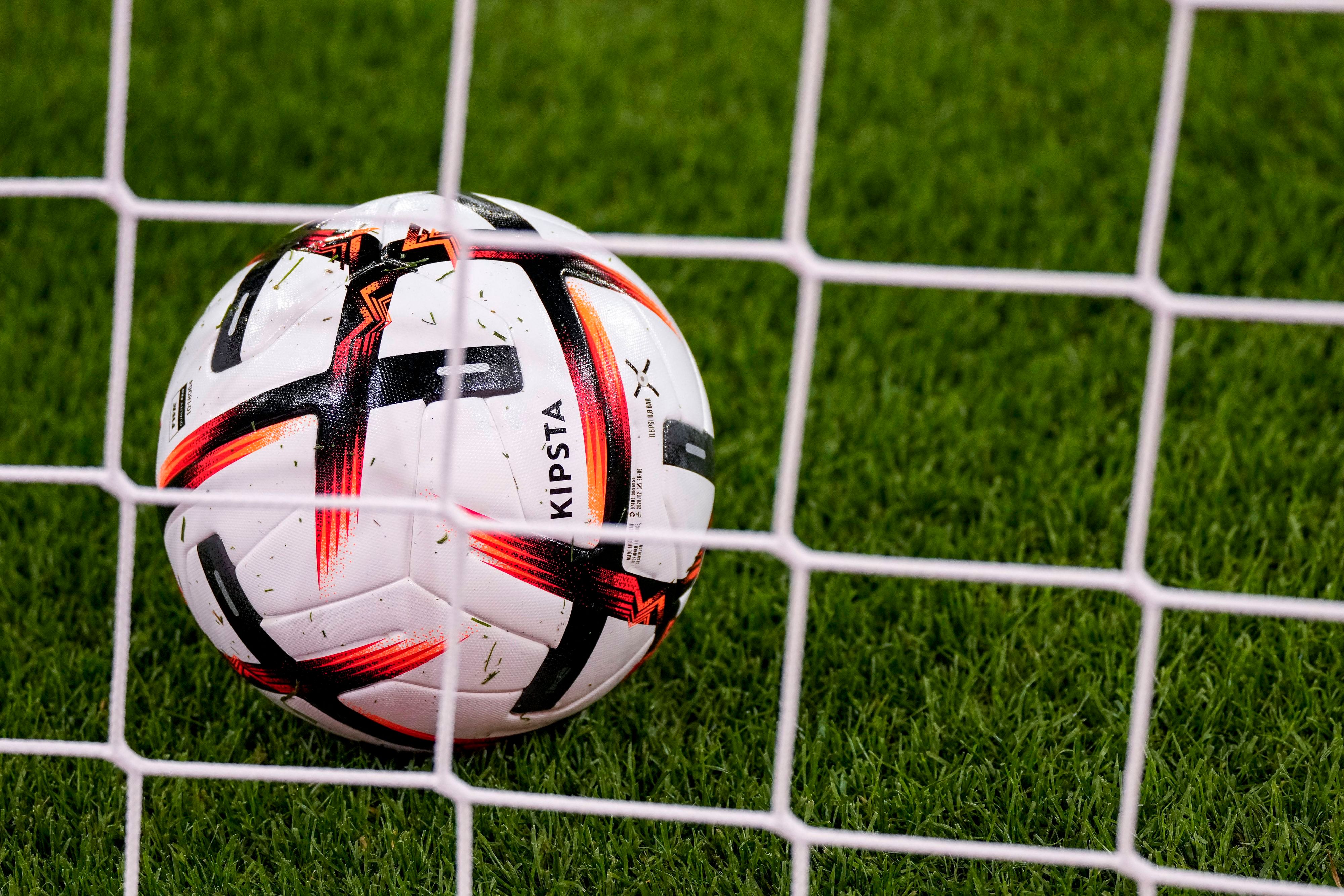 Ein Ball der Marke KIPSTA Decathlon Official Match Football liegt im Tor hinter dem Tornetz, offizieller Spielball, official Match Ball.