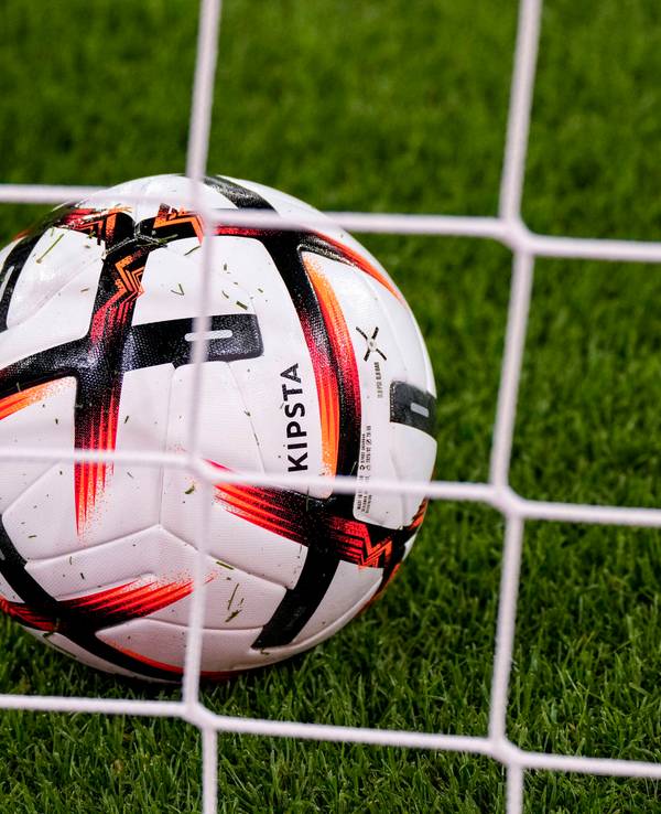 Ein Ball der Marke KIPSTA Decathlon Official Match Football liegt im Tor hinter dem Tornetz, offizieller Spielball, official Match Ball.