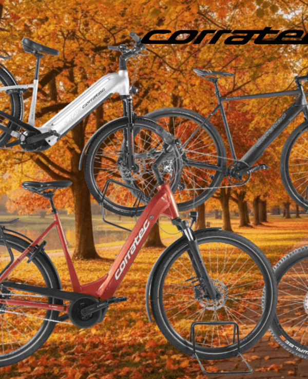 Mehrere Corratec E‑Bikes unterschiedlicher Typen – darunter Trekking-, City- und Mountainbikes – vor einer Landstraße an einem sonnigen Tag in Natur.
