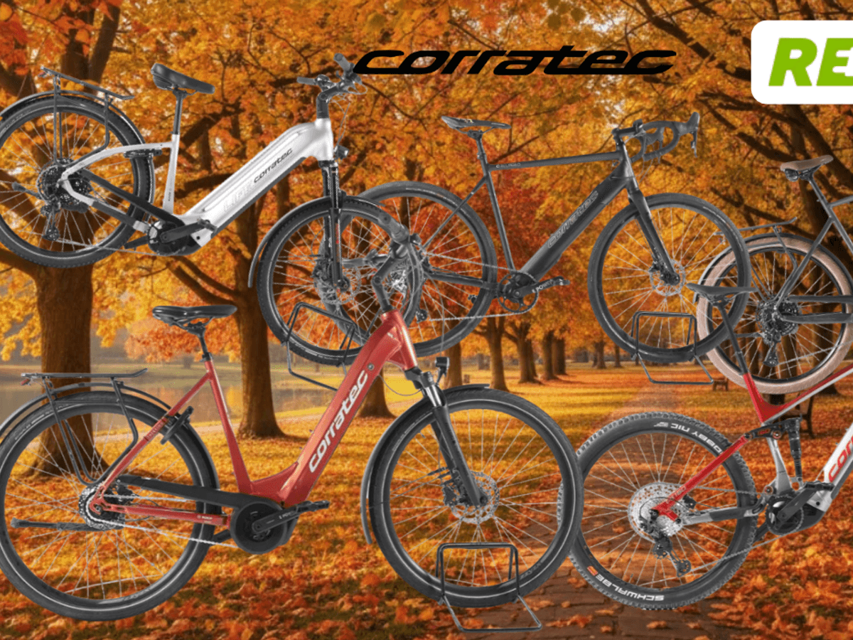 Mehrere Corratec E‑Bikes unterschiedlicher Typen – darunter Trekking-, City- und Mountainbikes – vor einer Landstraße an einem sonnigen Tag in Natur.