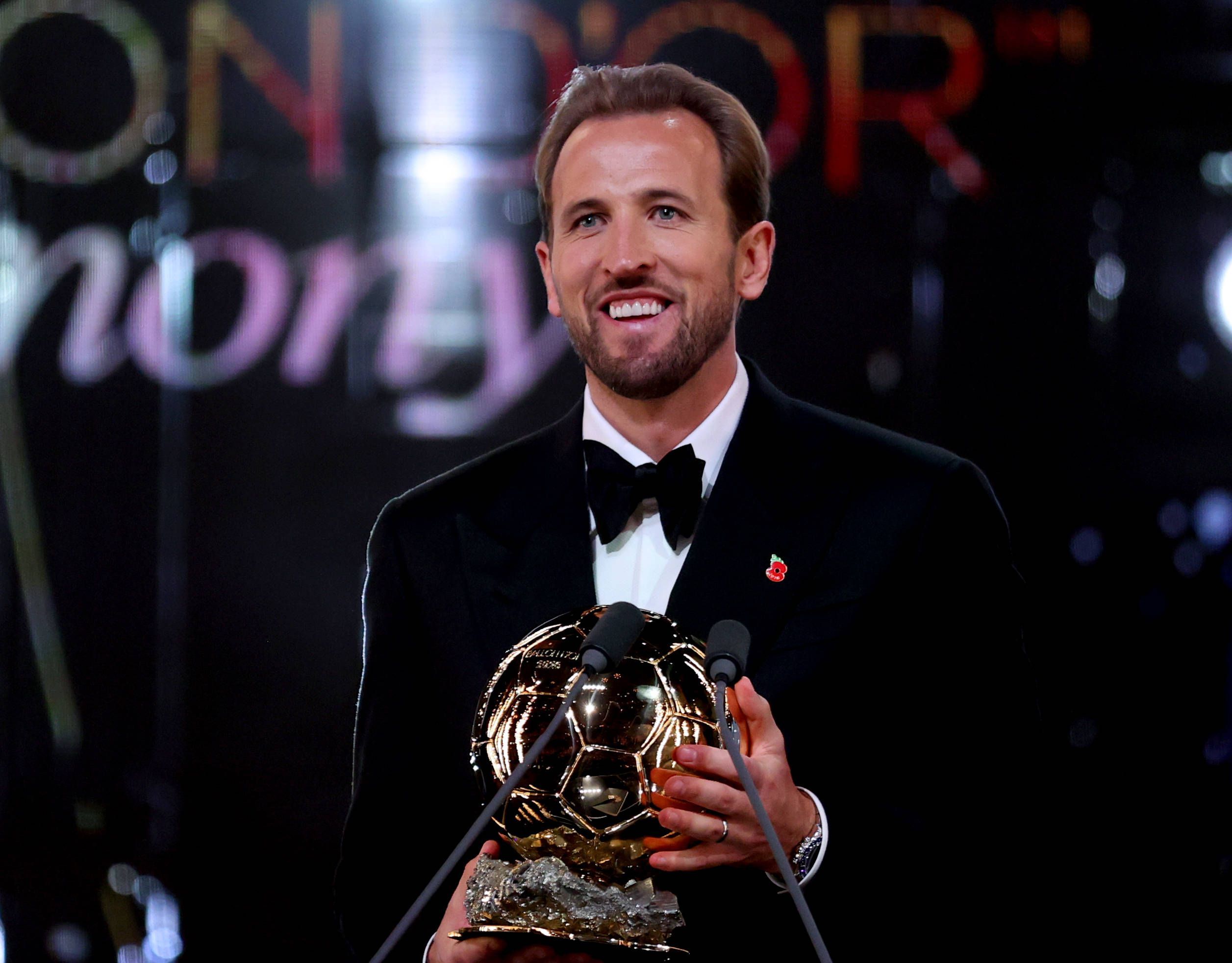Harry Kane lächelt mit der Ballon D`Or Trophäe in der Hand.