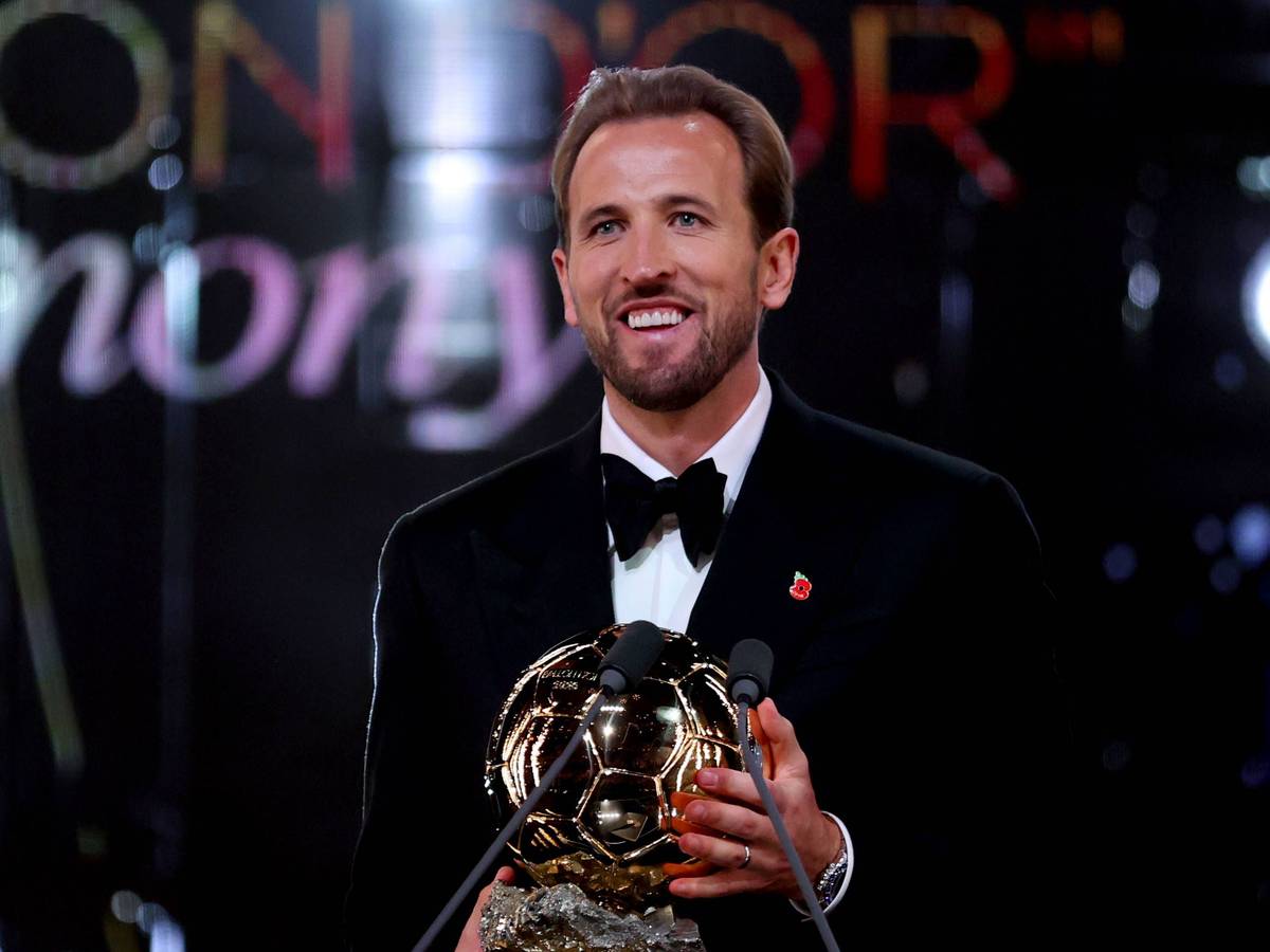Harry Kane lächelt mit der Ballon D`Or Trophäe in der Hand.