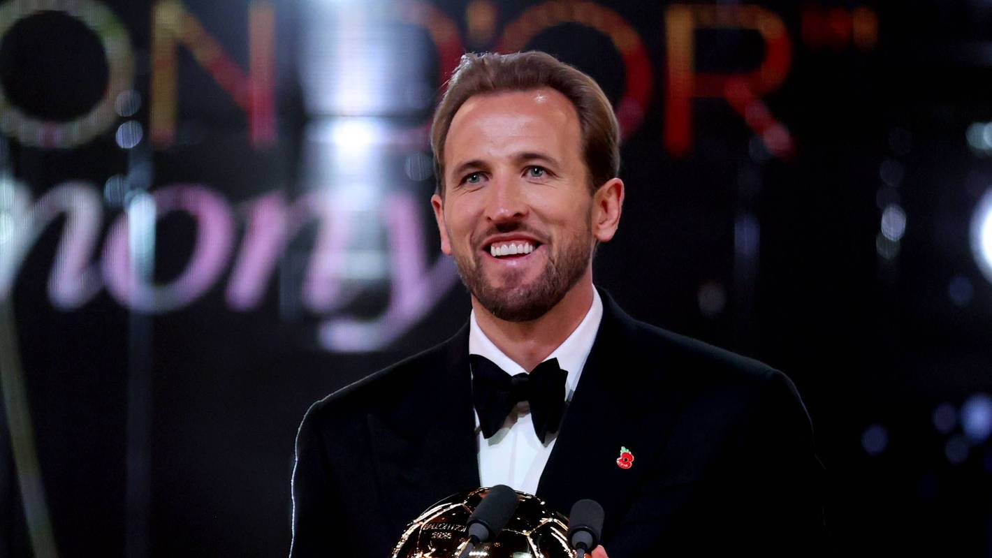 Harry Kane lächelt mit der Ballon D`Or Trophäe in der Hand.