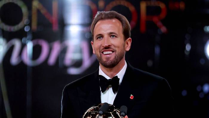 Harry Kane lächelt mit der Ballon D`Or Trophäe in der Hand.