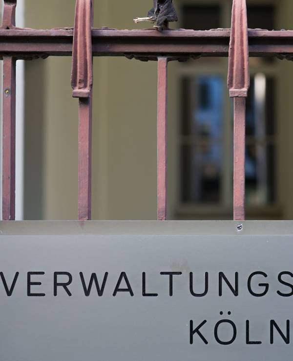 Ein Schild hängt am Eingang zum Verwaltungsgericht in Köln. +