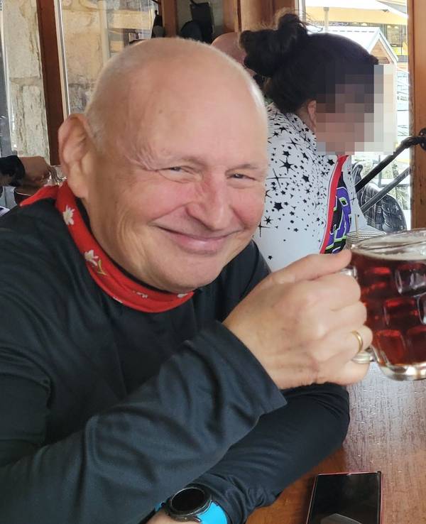 Zwei Männer sitzen an einem Tisch und stoßen mit Biergläsern an, im Hintergrund sitzen zwei Frauen.