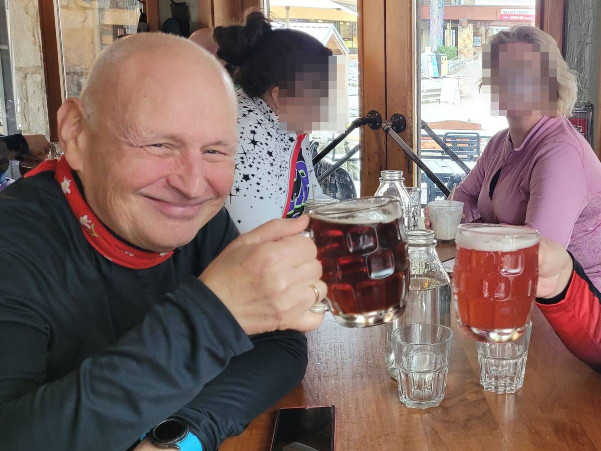 Zwei Männer sitzen an einem Tisch und stoßen mit Biergläsern an, im Hintergrund sitzen zwei Frauen.