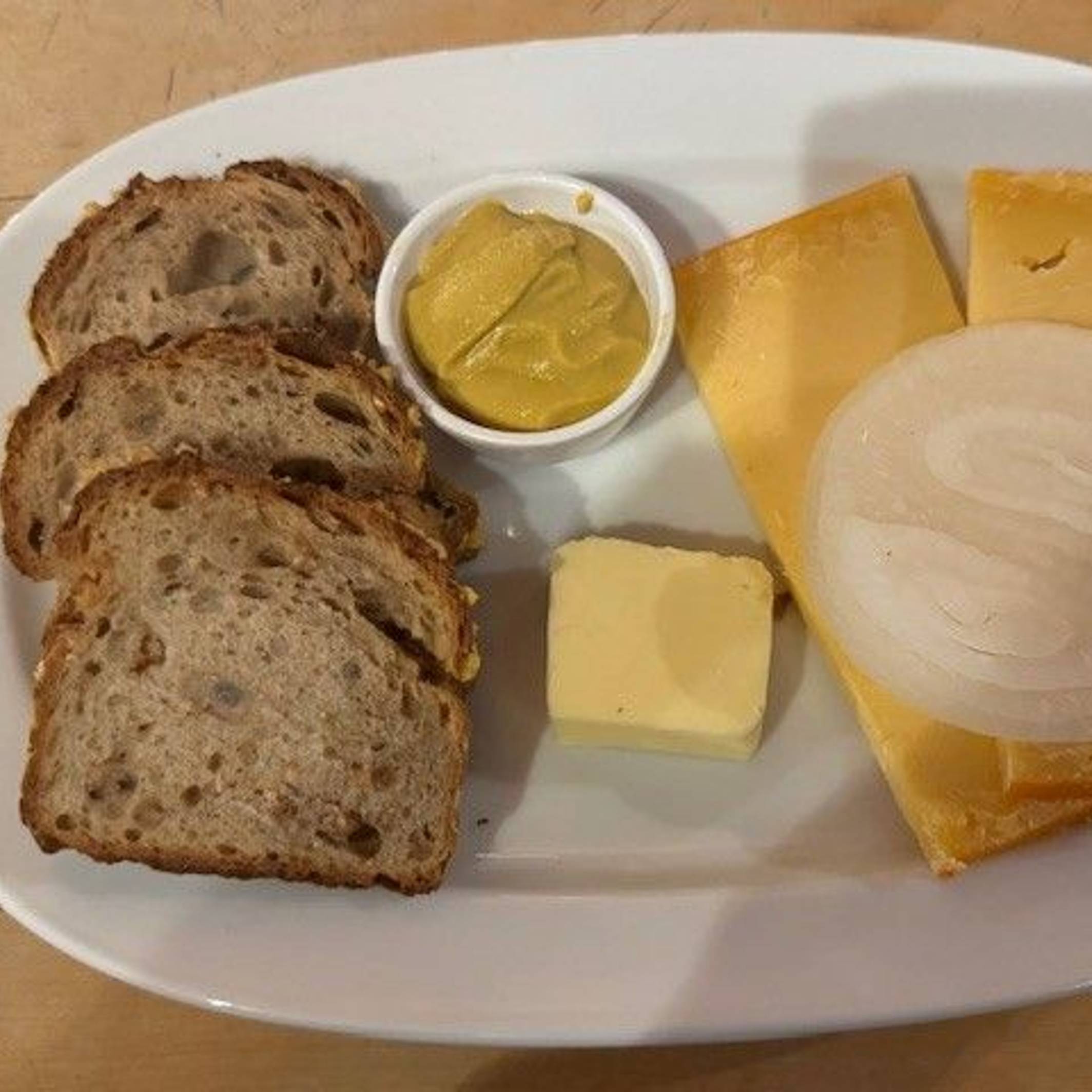 Auf einem Teller liegen drei Scheiben Brot, Butter, Senf und zwei Scheiben Käse mit Zwiebelringen