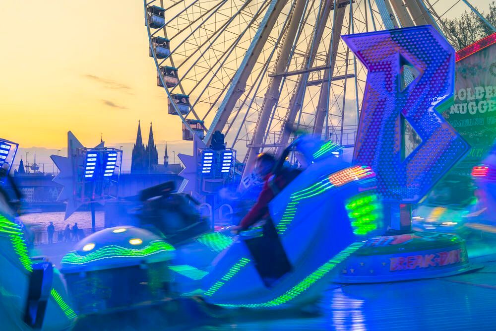 Ein leuchtendes Fahrgeschäft vor einem Riesenrad und dem Kölner Dom.