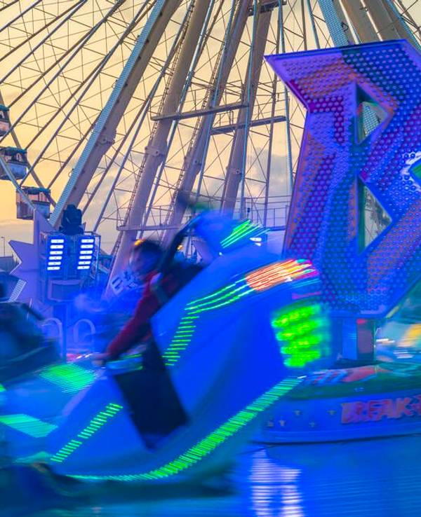 Ein leuchtendes Fahrgeschäft vor einem Riesenrad und dem Kölner Dom.