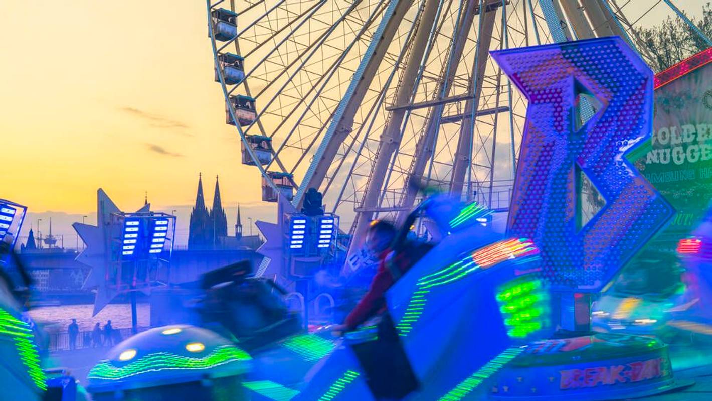 Ein leuchtendes Fahrgeschäft vor einem Riesenrad und dem Kölner Dom.