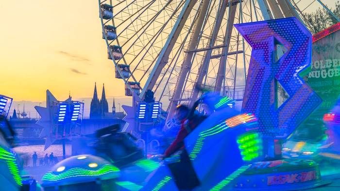 Ein leuchtendes Fahrgeschäft vor einem Riesenrad und dem Kölner Dom.