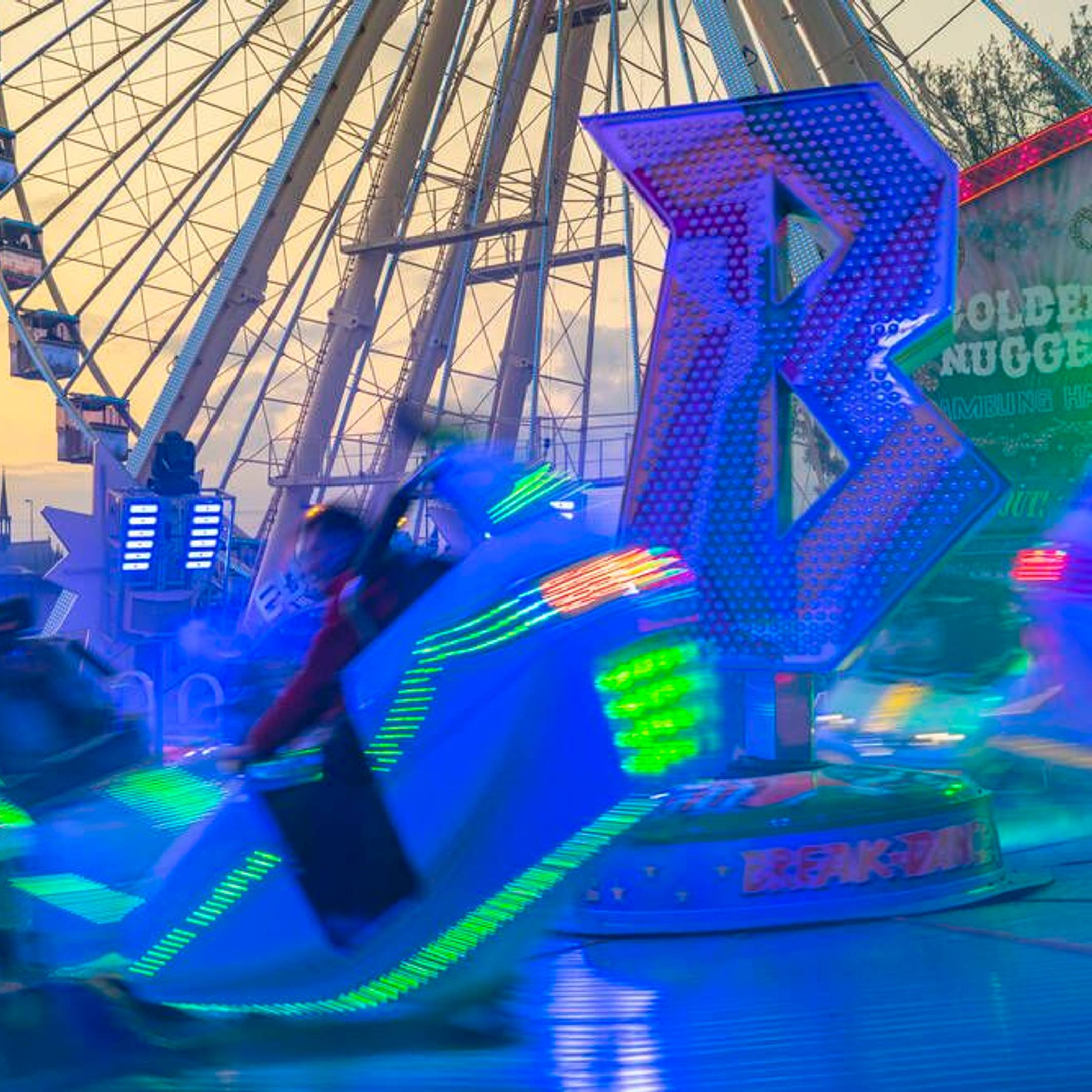 Ein leuchtendes Fahrgeschäft vor einem Riesenrad und dem Kölner Dom.