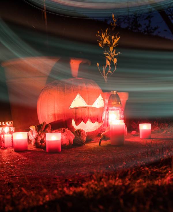 Um einen beleuchteten Halloween-Kürbis stehen Kerzen.