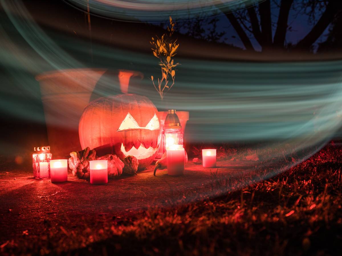 Um einen beleuchteten Halloween-Kürbis stehen Kerzen.