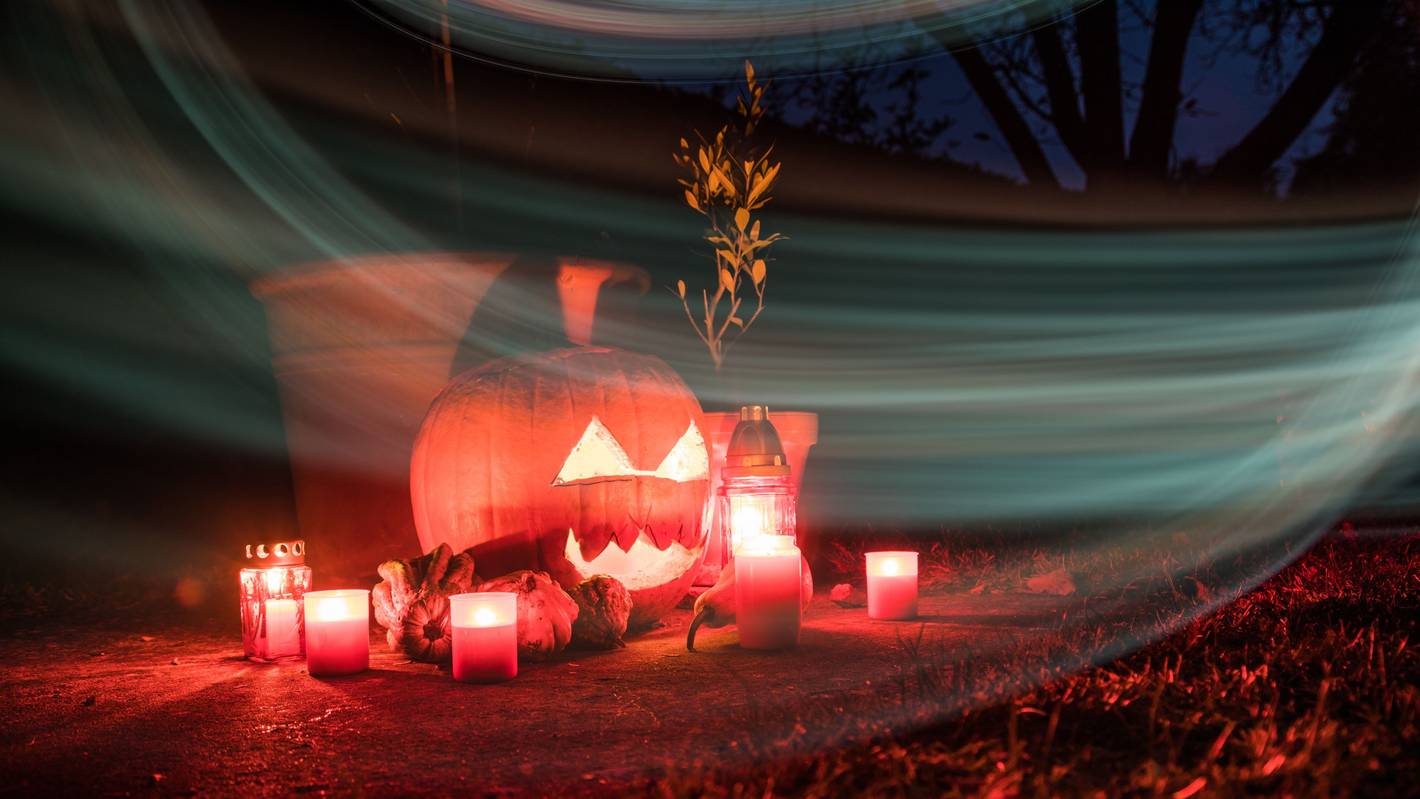 Um einen beleuchteten Halloween-Kürbis stehen Kerzen.