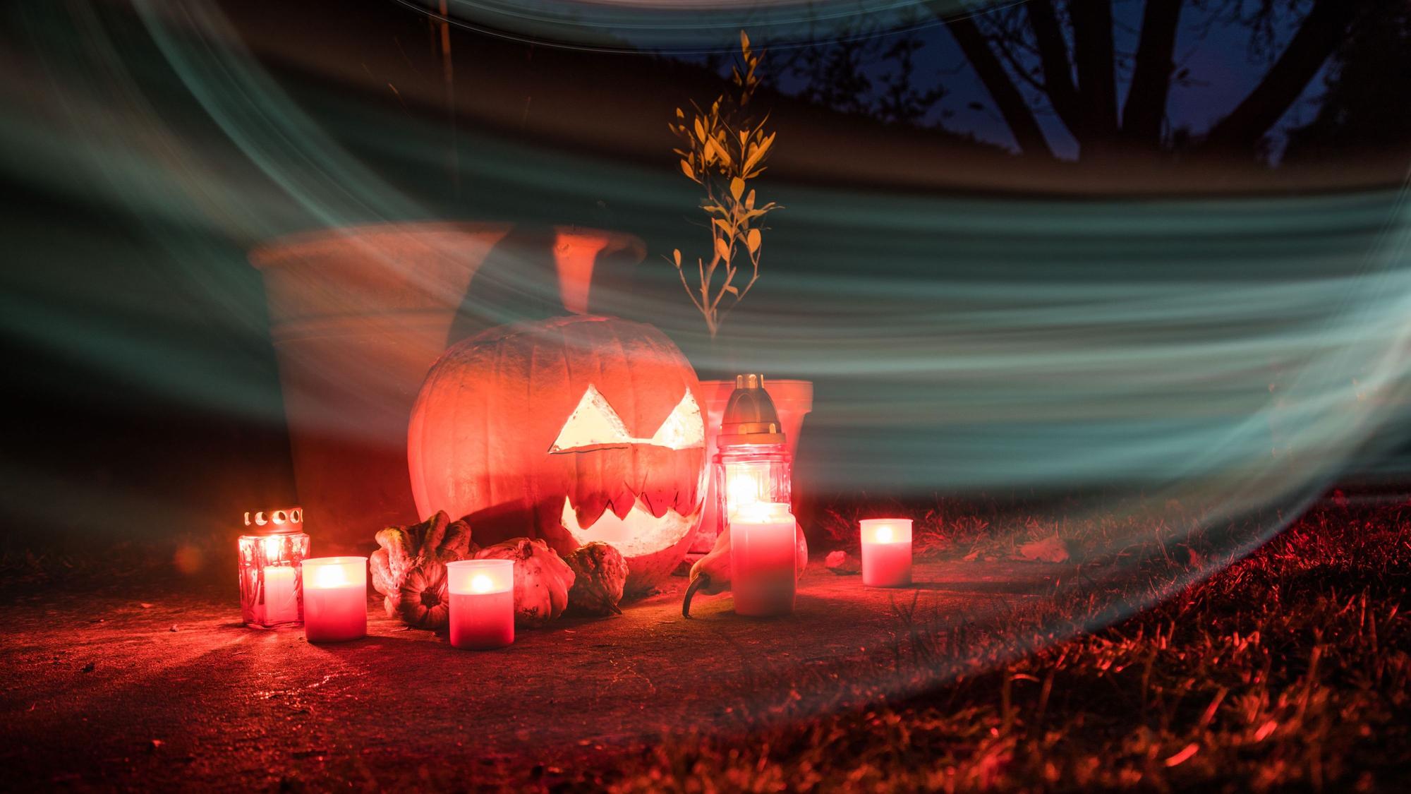 Um einen beleuchteten Halloween-Kürbis stehen Kerzen.