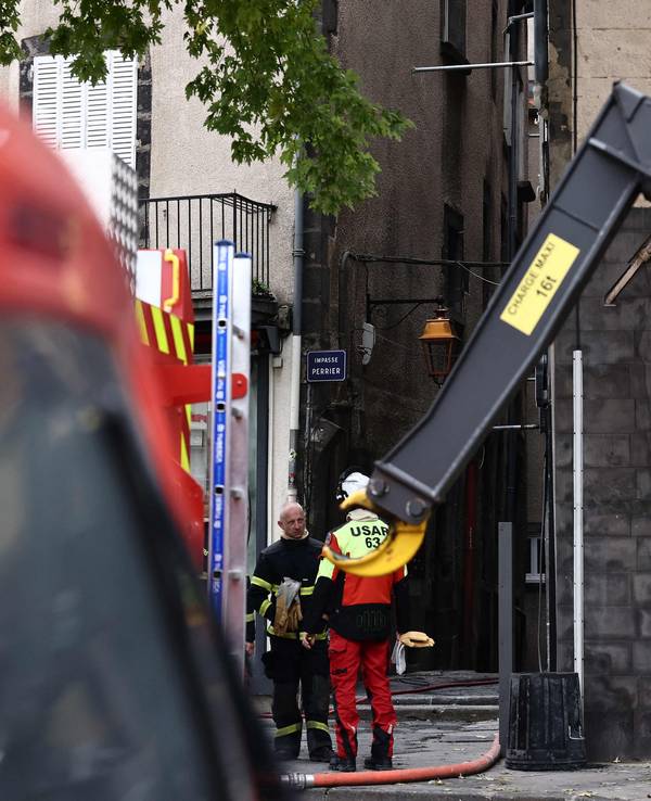 Zwei Feuerwehrmänner stehen an einem Haus, in dem es gebrannt hat.