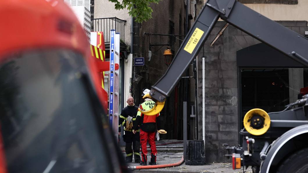 Zwei Feuerwehrmänner stehen an einem Haus, in dem es gebrannt hat.
