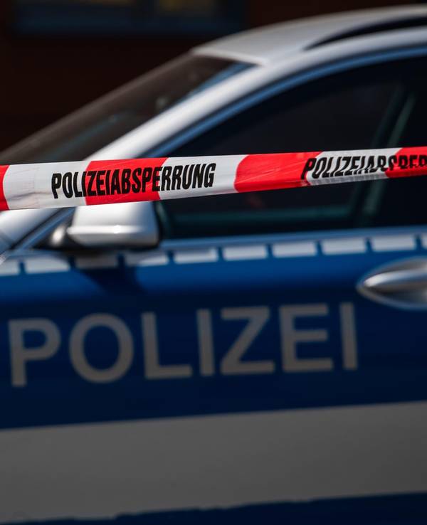 Ein Polizeiauto steht hinter einem Absperrband der Polizei.