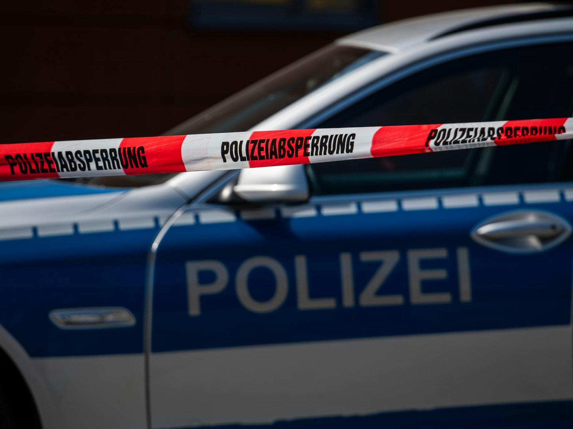 Ein Polizeiauto steht hinter einem Absperrband der Polizei.