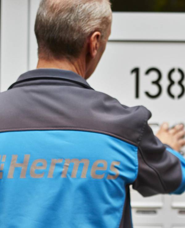Ein Hermes Paketbote klingelt an der Tür eines Wohnhauses.