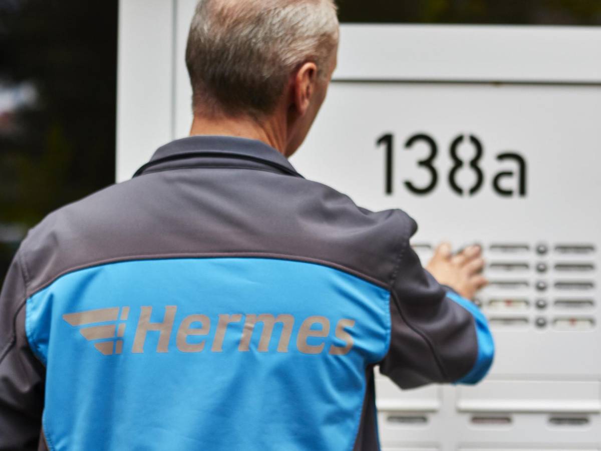 Ein Hermes Paketbote klingelt an der Tür eines Wohnhauses.