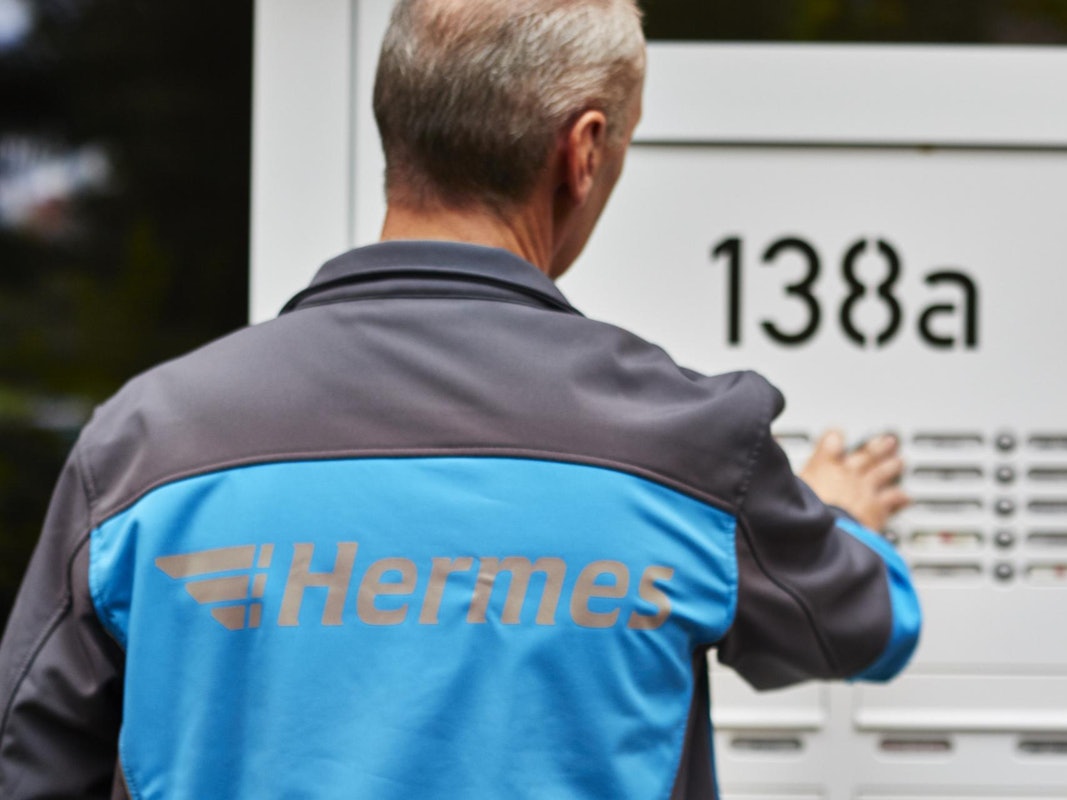 Ein Hermes Paketbote klingelt an der Tür eines Wohnhauses.