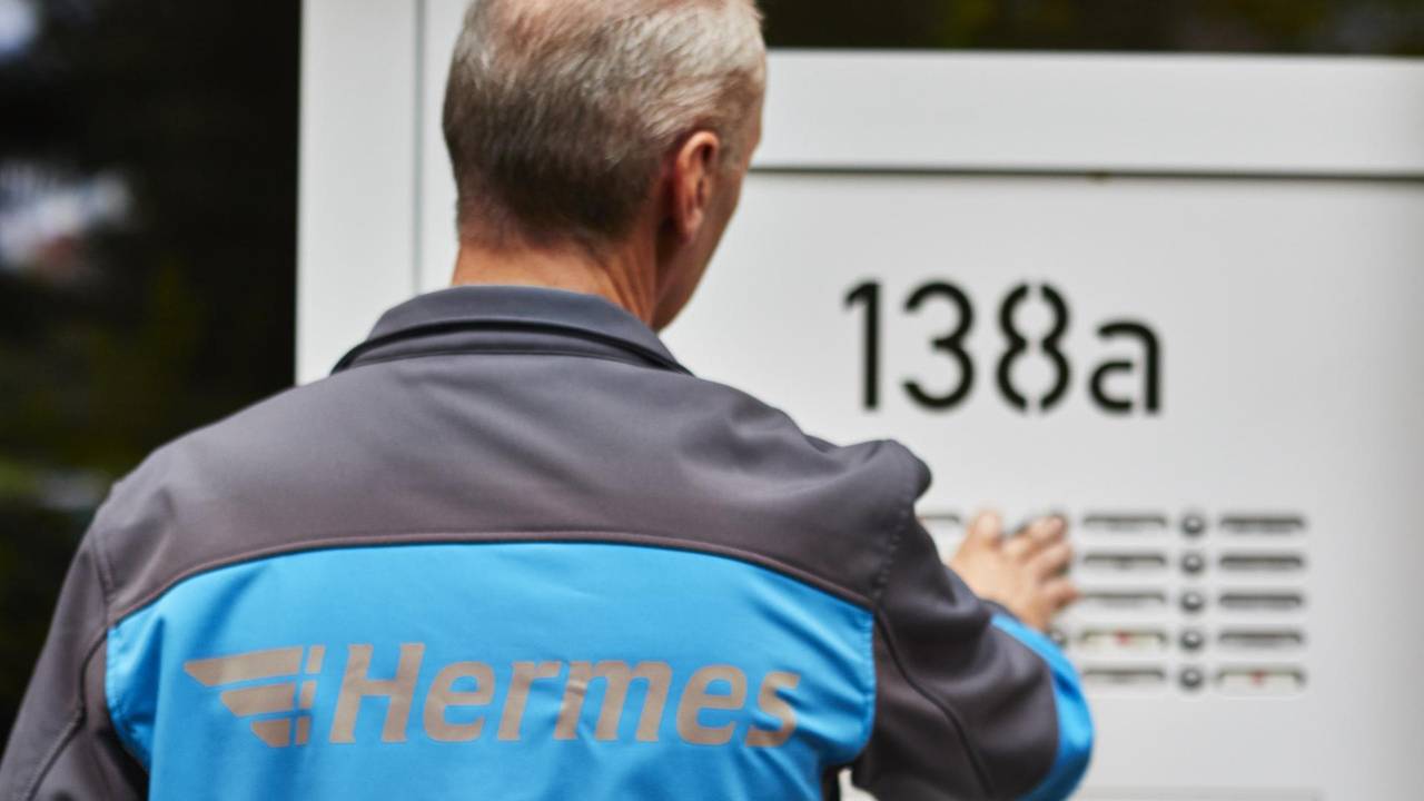 Ein Hermes Paketbote klingelt an der Tür eines Wohnhauses.