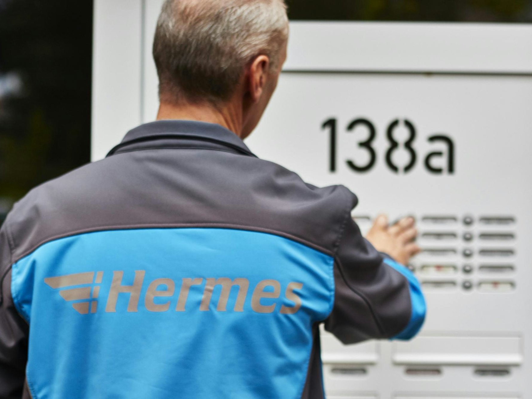 Ein Hermes Paketbote klingelt an der Tür eines Wohnhauses.
