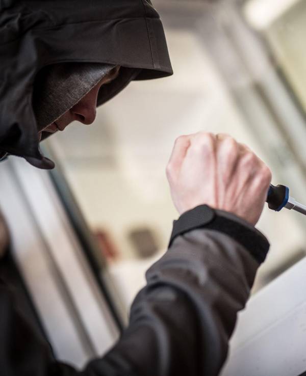 Ein Mann hebelt mit einem Schraubendreher ein Fenster auf.