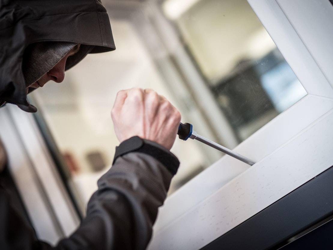 Ein Mann hebelt mit einem Schraubendreher ein Fenster auf.