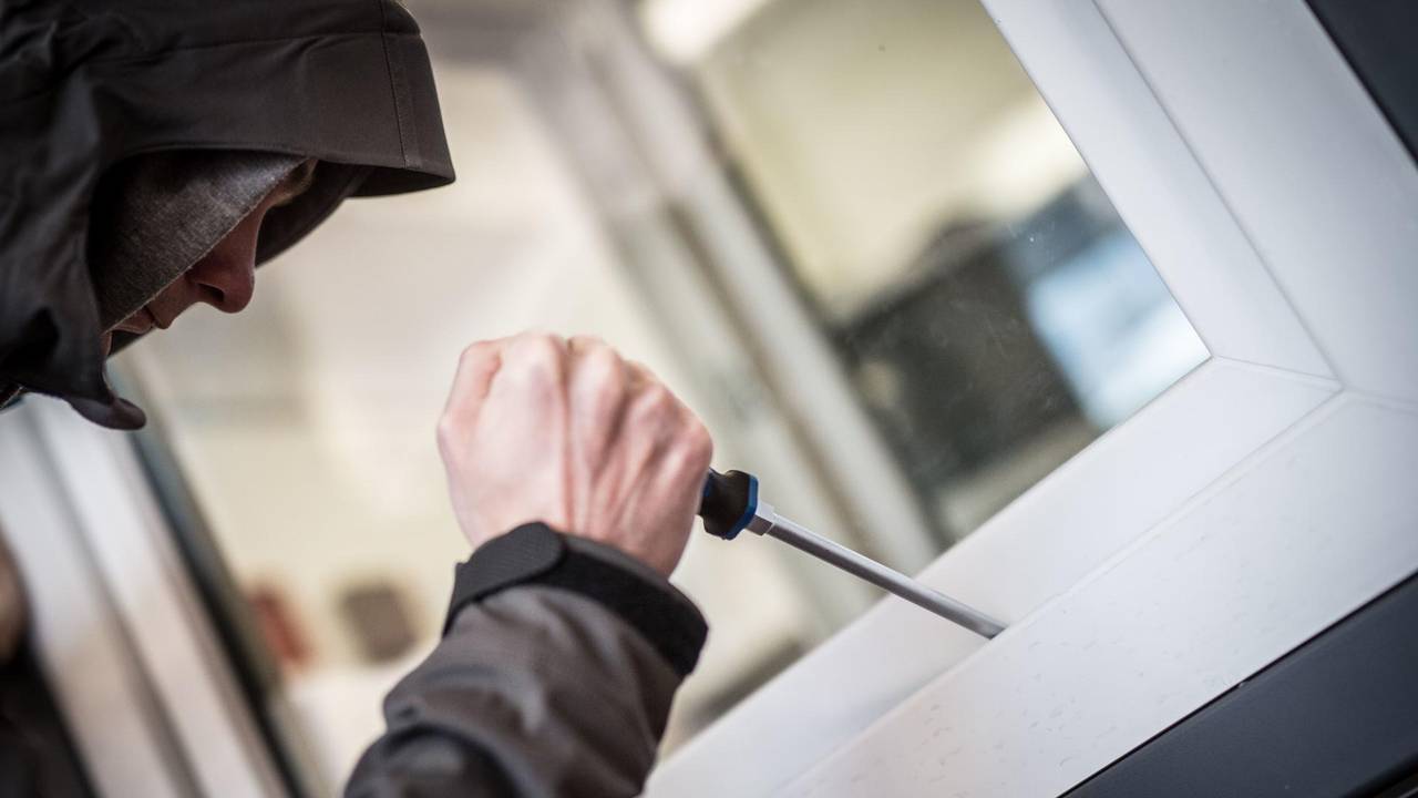Ein Mann hebelt mit einem Schraubendreher ein Fenster auf.