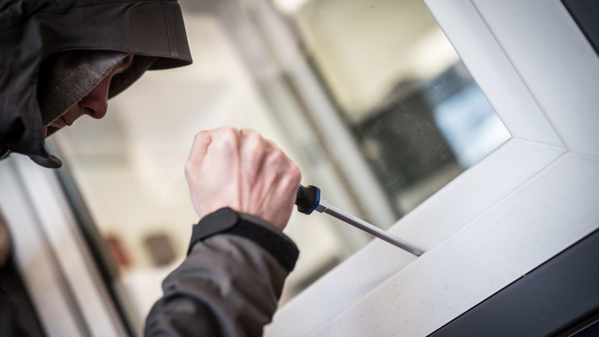 Ein Mann hebelt mit einem Schraubendreher ein Fenster auf.