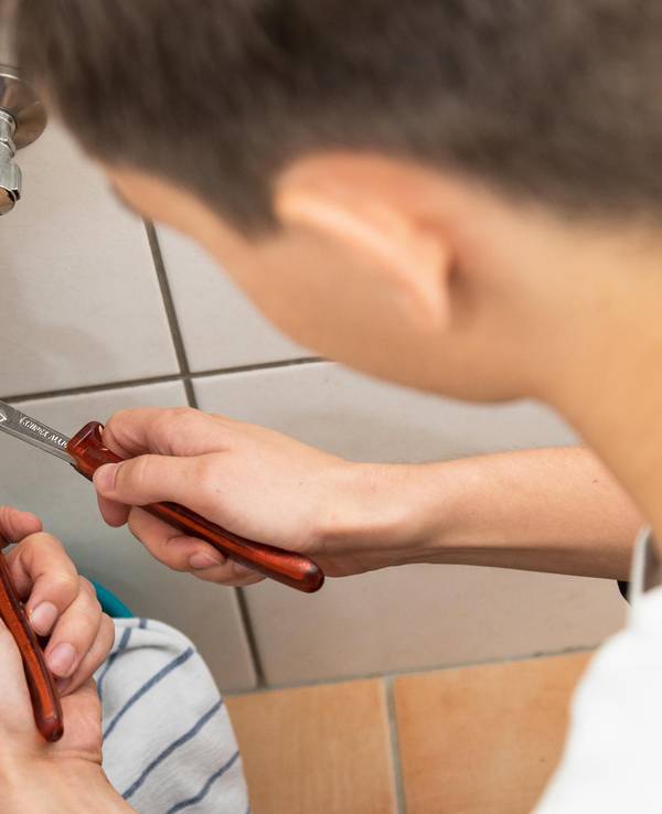 Das Symbolfoto zeigt einen Handwerker an einem Waschbeckenrohr.