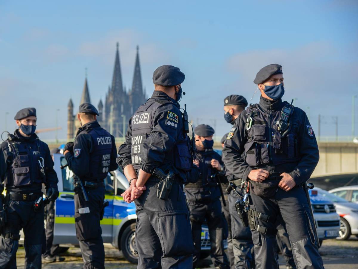 Mehrere Polizisten stehen vor mehreren Streifenwagen, im Hintergrund der Kölner Dom.