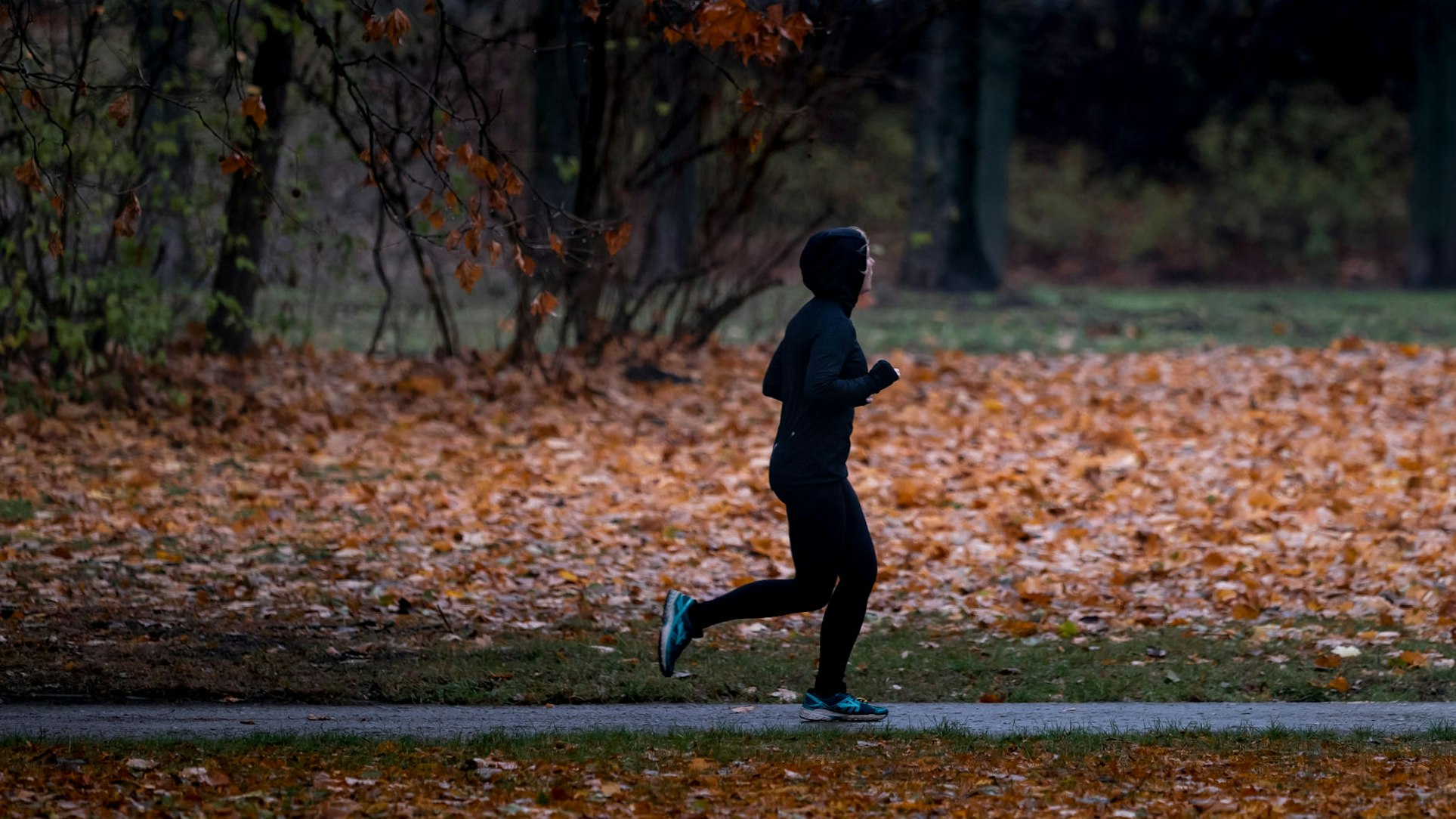 Eine Joggerin läuft bei Nieselregen durch einen Park.