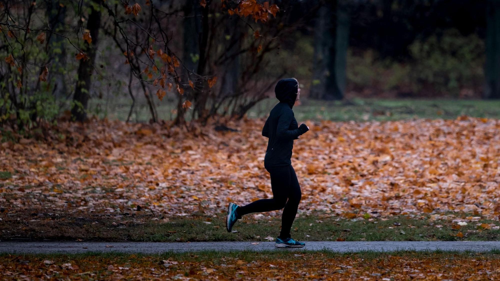 Eine Joggerin läuft bei Nieselregen durch einen Park.